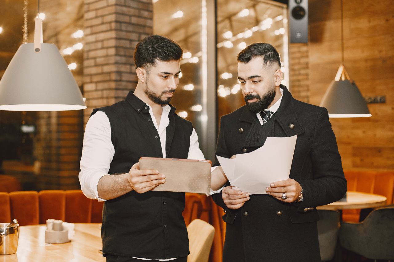 Two businessmen reviewing documents and a tablet in a modern indoor setting.